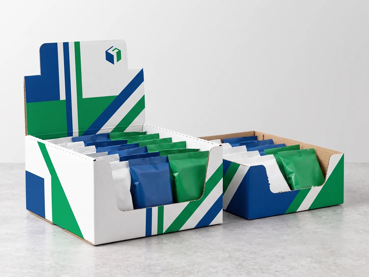 A printed counter display box in blue, green and white filled with small snack packs, beside a shelf-ready tray.