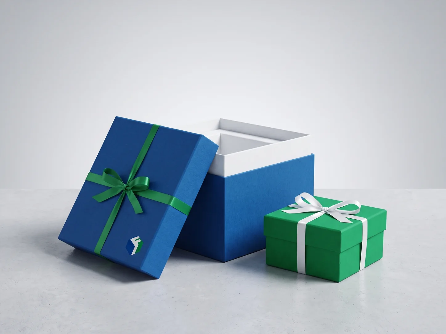 A rigid gift box wrapped in deep blue paper with a green ribbon, its lid lifted to show a white insert, beside a small green gift box.