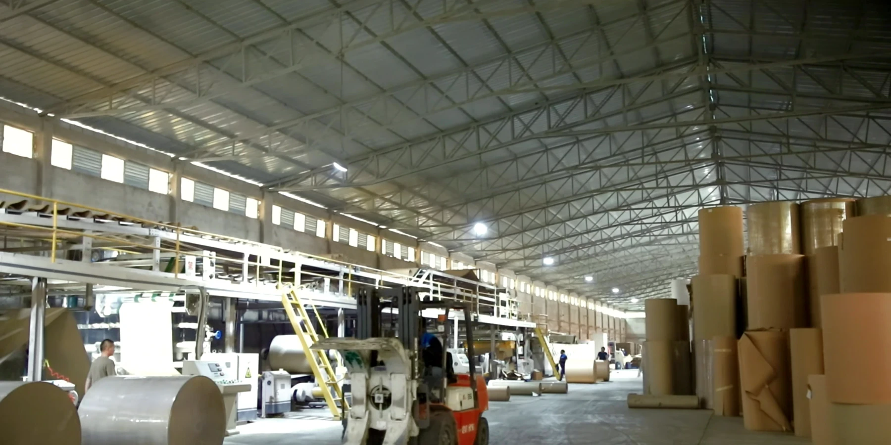 Wide view across the corrugating line, kraft reels and material-handling equipment.