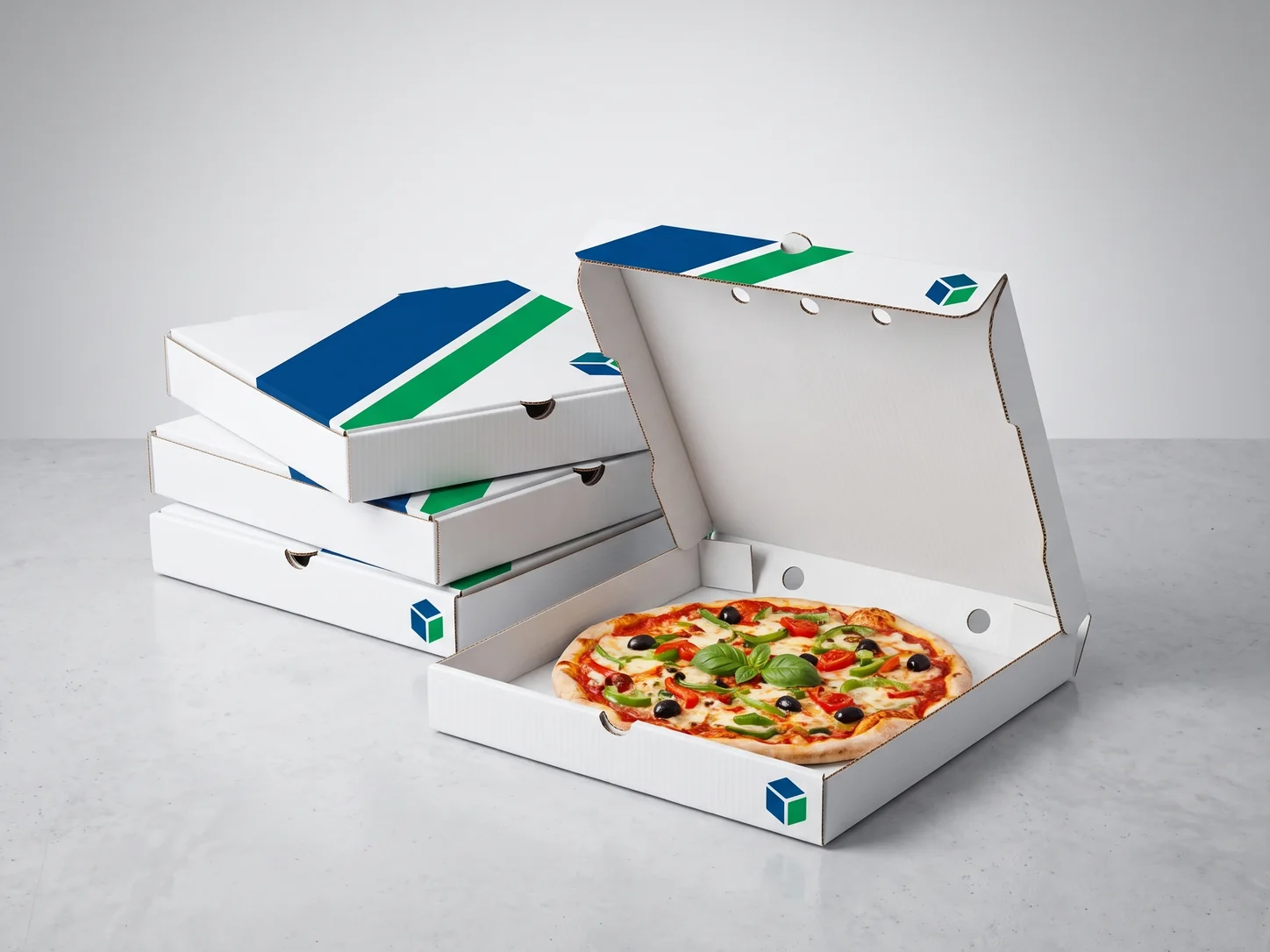 A stack of white corrugated pizza boxes printed with blue and green bands, beside an open box holding a vegetable pizza.